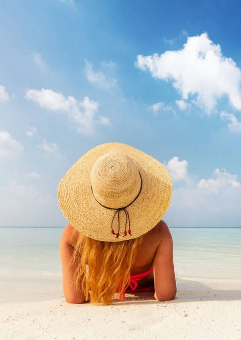 Beautiful young woman in sunhat lying relaxed on tropical beach in Maldives