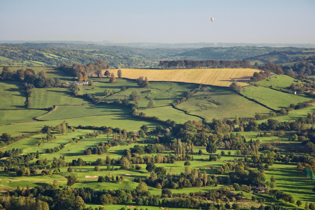 Aerial view of beautiful green countryside in Somerset, England. Includes fields, trees, golf course and a distant hot air balloon.