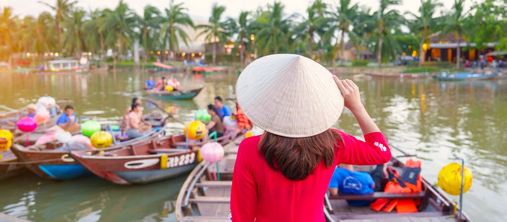 happy woman wearing Ao Dai Vietnamese dress, traveler visit Thu Bon River and Sightseeing Boat Ride at Hoi An ancient town. landmark for tourist attractions.Vietnam and Southeast travel concept